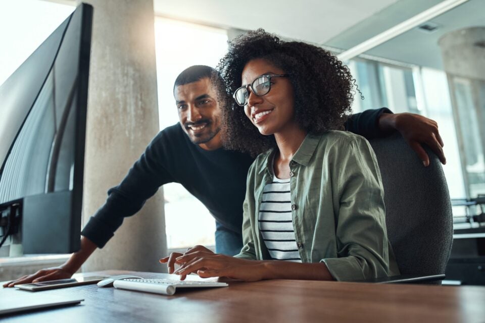 Image depicts two smiling people looking at a computer screen.