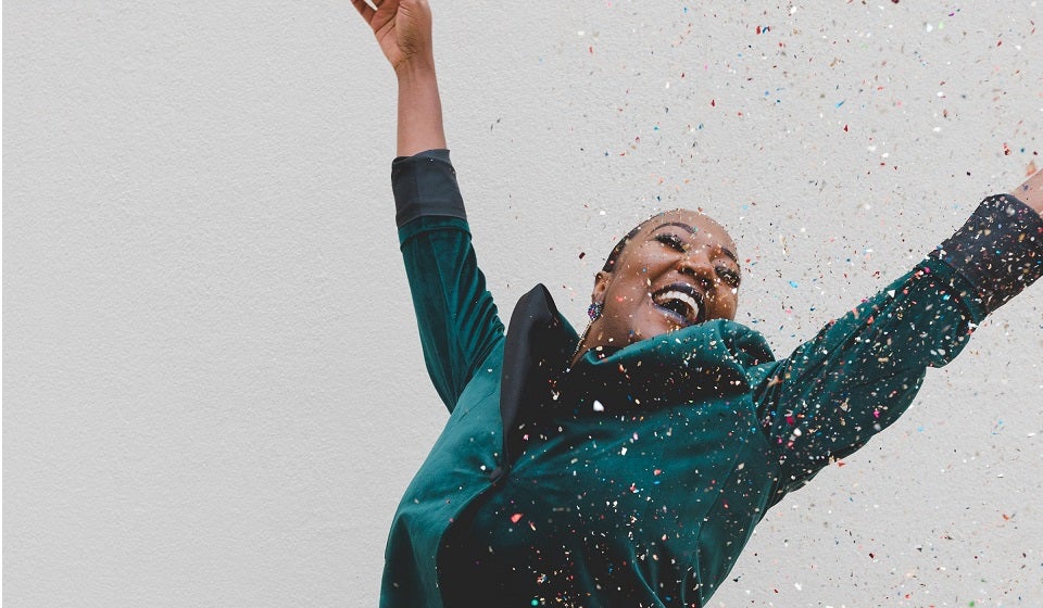 Black woman with arms up and confetti raining down