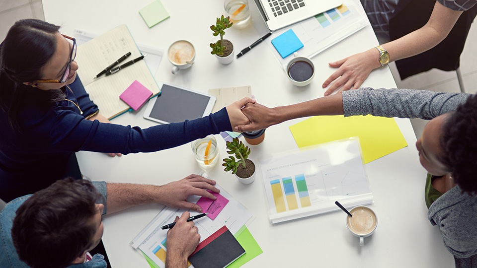 employees at a work table shaking hands colourful post-it notes and writing tools