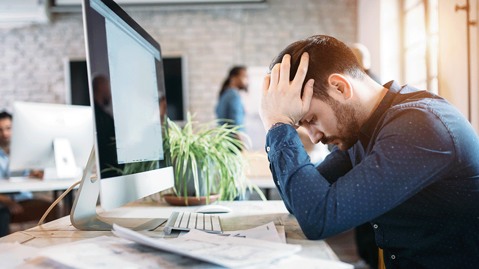man-sits-at-desk-modern-office-hands-in-head-looking-tired-frustrated