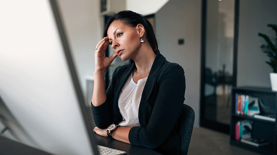 woamn-in-suit-at-large-computer-screen-hand=on=head-looks-stressed
